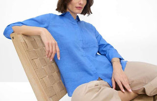 Woman in a casual blue blouse and beige pants sitting on a woven chair