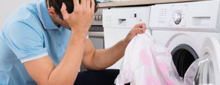 Man distressed holding color-stained shirt in front of washing machine, laundry accident