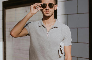 Man wearing a light gray short sleeve polo shirt and sunglasses in outdoor city setting