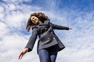 Woman outdoors in navy pea coat with gold buttons against a blue sky