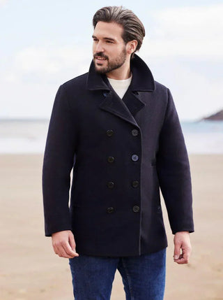 Man wearing a navy wool pea coat and jeans on a beach, winter men's fashion outerwear