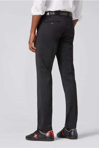 Man wearing slim fit black wool dress pants with black belt and black sneakers, rear view