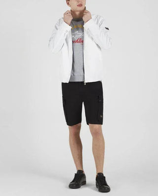 Man wearing white nylon jacket, grey graphic t-shirt, black cargo shorts, and black sneakers