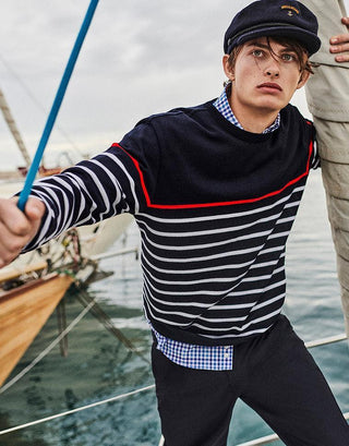 Man in navy striped sailor sweater and captain cap on a sailboat, nautical fashion style