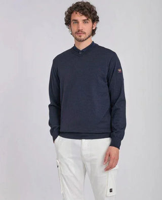 Man wearing navy V-neck merino wool sweater and white cargo pants against light background