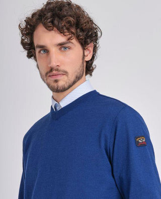 Man wearing blue merino wool V-neck sweater with patch on sleeve, light shirt underneath.