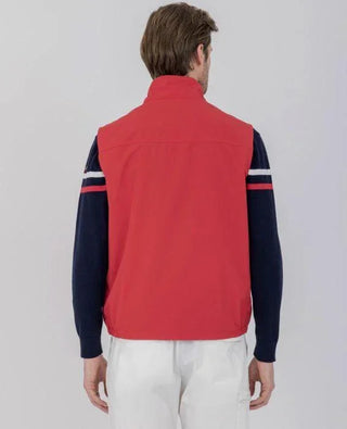 Man wearing red sleeveless nylon vest, navy sweater with stripes, and white pants, back view