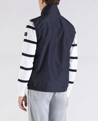 Man wearing navy nylon sleeveless vest over white sweater with navy stripes, back view