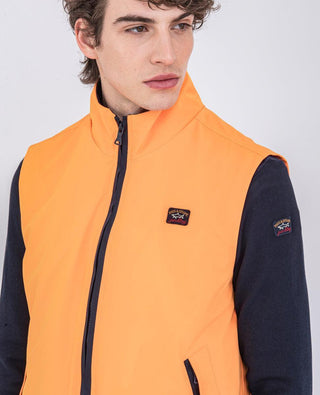 Man wearing an orange nylon sleeveless vest with zip and patch logo over a navy long-sleeve shirt
